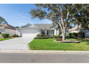 Charming single-story home featuring a well-manicured lawn, mature trees, and a two-car garage at 16950 Se 80Th Bellavista Cir, The Villages, FL 32162