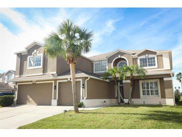 A two-story home with tan exterior, three car garage, manicured lawn and two palm trees at the front at 14126 Fox Glove St, Winter Garden, FL 34787