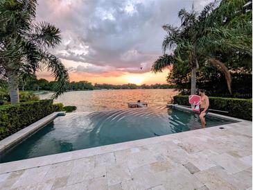 Sunset view from the pool overlooking the lake, enhanced by travertine pavers and lush, mature palm trees at 1010 Strathmore Dr, Orlando, FL 32806