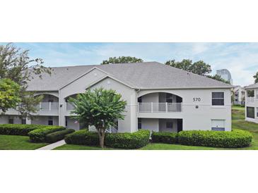 Exterior view of the property featuring white facade, grey roof, well-manicured lawn and mature trees at 570 Cranes Way # 248, Altamonte Springs, FL 32701