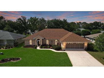 Charming single-story home featuring a well-manicured lawn and a screened two-car garage at sunset at 5825 Princess Caroline Pl, Leesburg, FL 34748