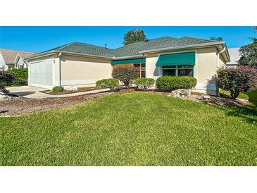 Cream-colored home featuring a well-manicured lawn, tasteful landscaping, and green awnings over the windows at 3049 Glenwood Pl, The Villages, FL 32162