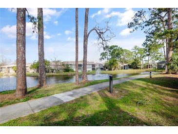 Scenic view of community lake with fountain, mature trees, sidewalk, and building in the background at 5783 Peregrine Ave # C07, Orlando, FL 32819