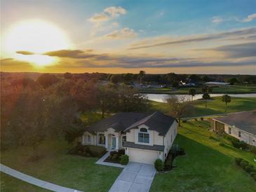 Stunning property with golf course and pond views, lush landscaping, and welcoming curb appeal during sunset at 36711 Alaqua Ct, Eustis, FL 32736