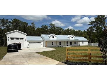 Stunning exterior view of a modern farmhouse with a well-manicured lawn and a long private driveway at 12009 Sw 61St Place Road, Ocala, FL 34481