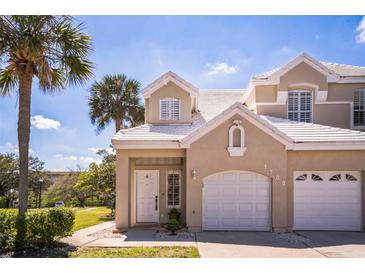 Charming townhouse featuring a two-car garage, white tile roof, and tropical landscaping at 7700 Carriage Homes Dr # 4, Orlando, FL 32819