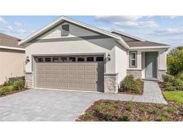 Charming single-Gathering home with a two-car garage, neutral stucco, stone accents, and a well-manicured lawn at 9116 Wildlight Trl, Wildwood, FL 34785