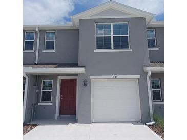 Two-story home with gray siding, red door, a white garage door, and well-maintained front yard at 545 Zinfandel Dr, Holly Hill, FL 32117
