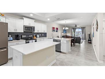 Modern kitchen with white cabinetry, stainless appliances, and an island featuring light countertops and an open concept living area at 4721 Clock Tower Dr # 204, Kissimmee, FL 34746