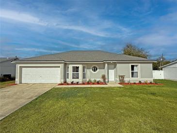 Charming single-story home featuring manicured lawn, flower beds, a gray roof, and a two-car garage at 3258 Cranston St, Deltona, FL 32738