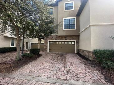 Townhouse exterior featuring a two-car garage with brick paver driveway and stone accents at 1341 Shinnecock Hills Dr, Davenport, FL 33896