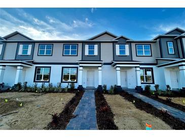 Modern three-story townhome with gray and white siding, and a brick walkway at 592 Pothos St, Apopka, FL 32703