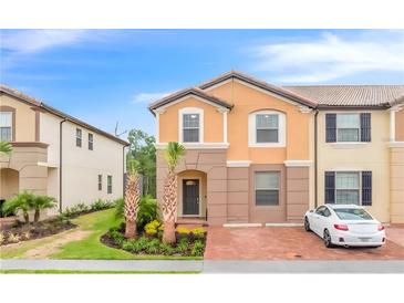 Two-story townhome with orange exterior, landscaping, and a driveway at 8851 Geneve Ct, Kissimmee, FL 34747