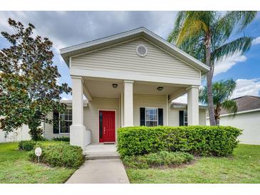 Beige house with red door, covered porch, and manicured landscaping at 4973 Pall Mall W St, Kissimmee, FL 34758