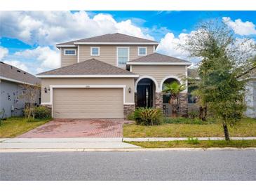 Two-story house with tan siding, a two-car garage, and a brick paver driveway at 285 Miro Dr, Davenport, FL 33837