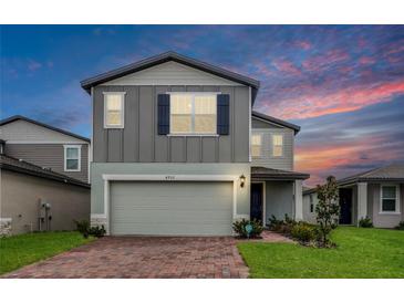 Two-story home with a brick driveway, manicured lawn, and a gray exterior with blue shutters at 4932 Mainsail St, Haines City, FL 33844