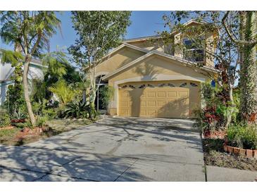 Two story tan house with a large garage surrounded by well manicured landscaping at 2981 Viscount Cir, Kissimmee, FL 34747