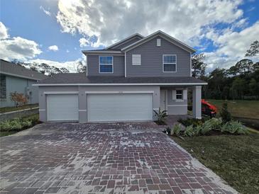 Two-story house with gray siding, three-car garage, and a brick-paver driveway at 1696 Andover Ridge Dr, Deland, FL 32720