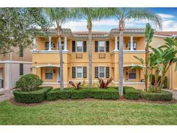 Two-story townhome with yellow exterior, lush landscaping, and palm trees at 8451 Leatherleaf Ln, Orlando, FL 32827