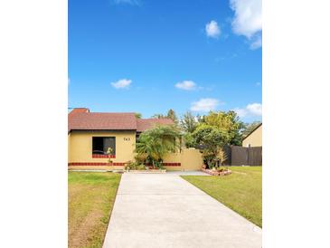 Cute yellow house with red tile roof, landscaped yard, and concrete driveway at 743 Golden Sunshine Cir, Orlando, FL 32807