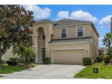 Two-story house with beige exterior, a large garage, and lush landscaping at 7773 Basnett Cir, Kissimmee, FL 34747