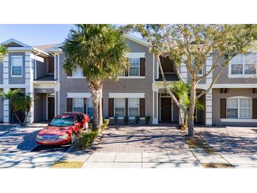 Two-story townhome with gray siding, paver driveway, and palm trees at 2394 Caravelle Cir, Kissimmee, FL 34746