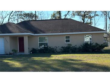 Tan house with brown roof, red door, and well-manicured lawn at 7047 Sw 131St Loop, Ocala, FL 34473