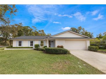 Ranch style home with white brick exterior, attached garage, and well-manicured lawn at 7884 Broken Arrow Trl, Winter Park, FL 32792