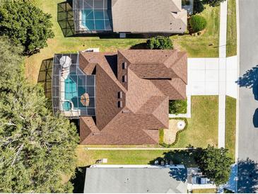 Aerial view of a home with a screened in pool, well-manicured lawn, and brown shingled roof at 13132 Coldwater Loop, Clermont, FL 34711