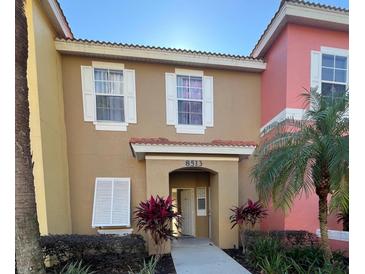 Two-story townhome with tan and pink exterior, landscaping, and walkway at 8513 Crystal Cove Loop, Kissimmee, FL 34747