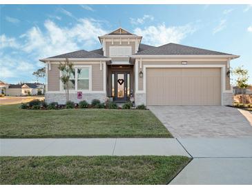 Tan two-story house with a three-car garage and landscaped lawn at 8575 Hempstead Way, Mount Dora, FL 32757