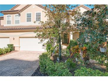 Tan three-story townhome with two-car garage, landscaping, and brick driveway at 8737 The Esplanade # 65, Orlando, FL 32836
