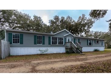 Gray manufactured home with white skirting, wooden steps, and a long driveway at 13811 County Road 109D, Lady Lake, FL 32159