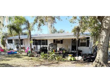 White doublewide mobile home with covered porch, large backyard, and mature trees at 475 80 Foot Rd, Bartow, FL 33830