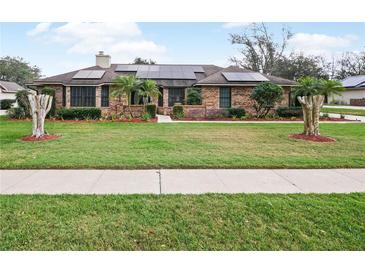 Charming brick home featuring manicured lawn, decorative trees and solar panels on the roof at 647 Saranac Dr, Winter Springs, FL 32708