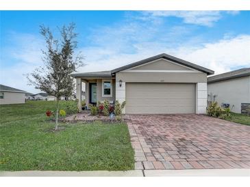 Beige house with a gray roof, two-car garage, and a brick paver driveway at 4451 Rapallo Ave, Winter Haven, FL 33884