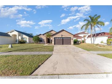 Tan house with brown double garage door, green lawn, and palm trees at 2463 Hybrid Dr, Kissimmee, FL 34758