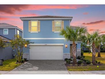 Two-story light blue house with a white garage door and landscaping at 7260 Oakmoss Loop, Davenport, FL 33837