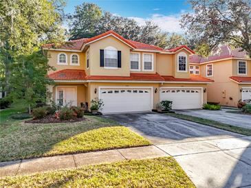 Tan two-story townhome with red tile roof, two-car garage, and landscaped yard at 2244 N Wekiva Village Ln, Apopka, FL 32703