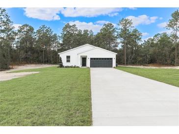 White farmhouse exterior with black garage door and landscaping at 7542 Sw 128 Terrace Rd, Dunnellon, FL 34432