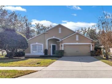 Tan one-story house with two-car garage and lush landscaping at 900 Khingan Ct, Apopka, FL 32712