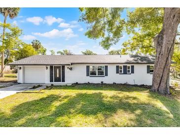 Charming single-story white brick home featuring manicured lawn and lush landscaping and dark trim at 720 Jasmine Ave, Orange City, FL 32763