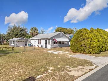 Gray house with a white garage and American flag, surrounded by a grassy yard and chain link fence at 1119 Pine Ave, Tavares, FL 32778