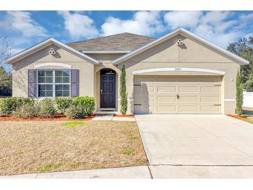 Tan house with gray roof, landscaping, and two-car garage at 2860 Ne 42Nd Rd, Ocala, FL 34470