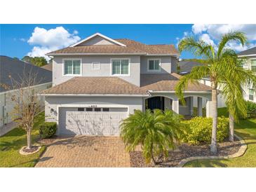 Charming two-story home with a well-manicured lawn, brick driveway, and lush landscaping with palm trees at 4455 Indigo Sky Ln, Kissimmee, FL 34744