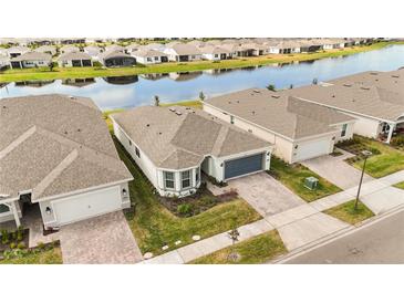 Aerial view of a modern single-Gathering home in a waterfront community with lush landscaping and a gray colored driveway and garage door at 2496 Pine Preserve Ct, St Cloud, FL 34771