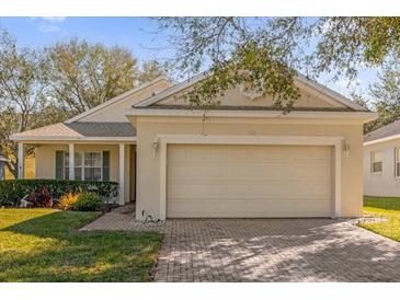Beige home featuring a two-car garage and a brick paver driveway, with manicured landscaping and inviting curb appeal at 2513 Castle Pines St, Clermont, FL 34711