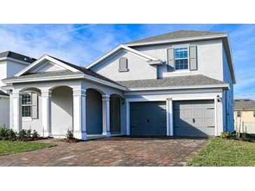 Two-story home features a gray exterior, arched entryway, brick driveway, and a two-car garage at 4425 Lions Gate Ave, Clermont, FL 34711