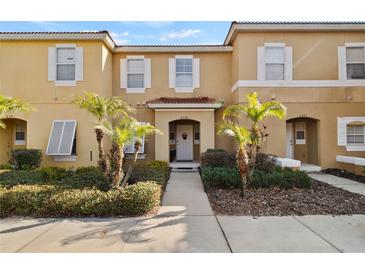 Two-story townhome with light beige exterior, walkway, and tropical landscaping at 8543 Bay Lilly Loop, Kissimmee, FL 34747