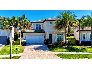 Two-story home featuring a two-car garage, stone accents, well-manicured lawn, and mature palm trees at 10680 Royal Cypress Way, Orlando, FL 32836